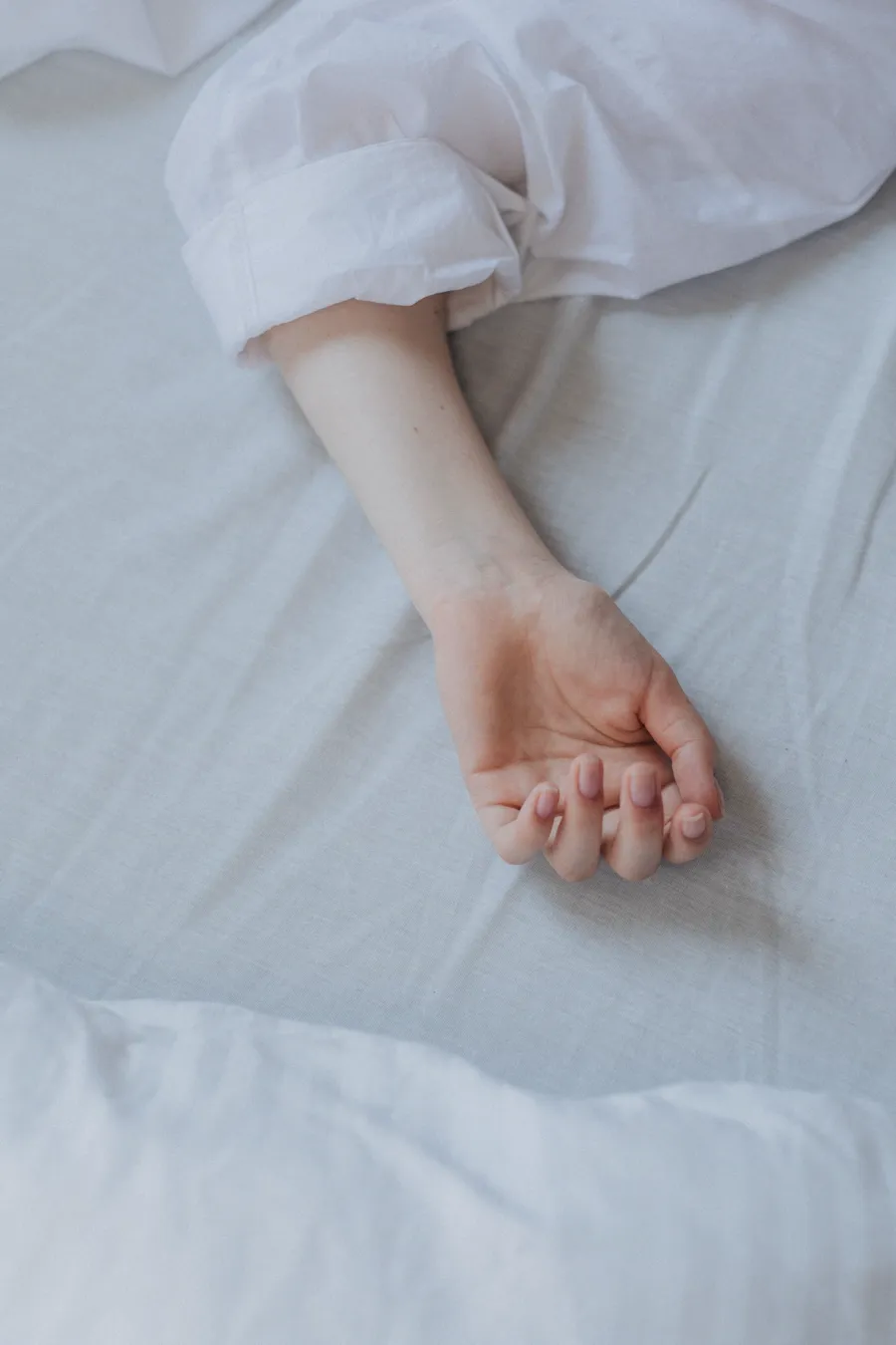Mão repousando sobre roupa de cama branca