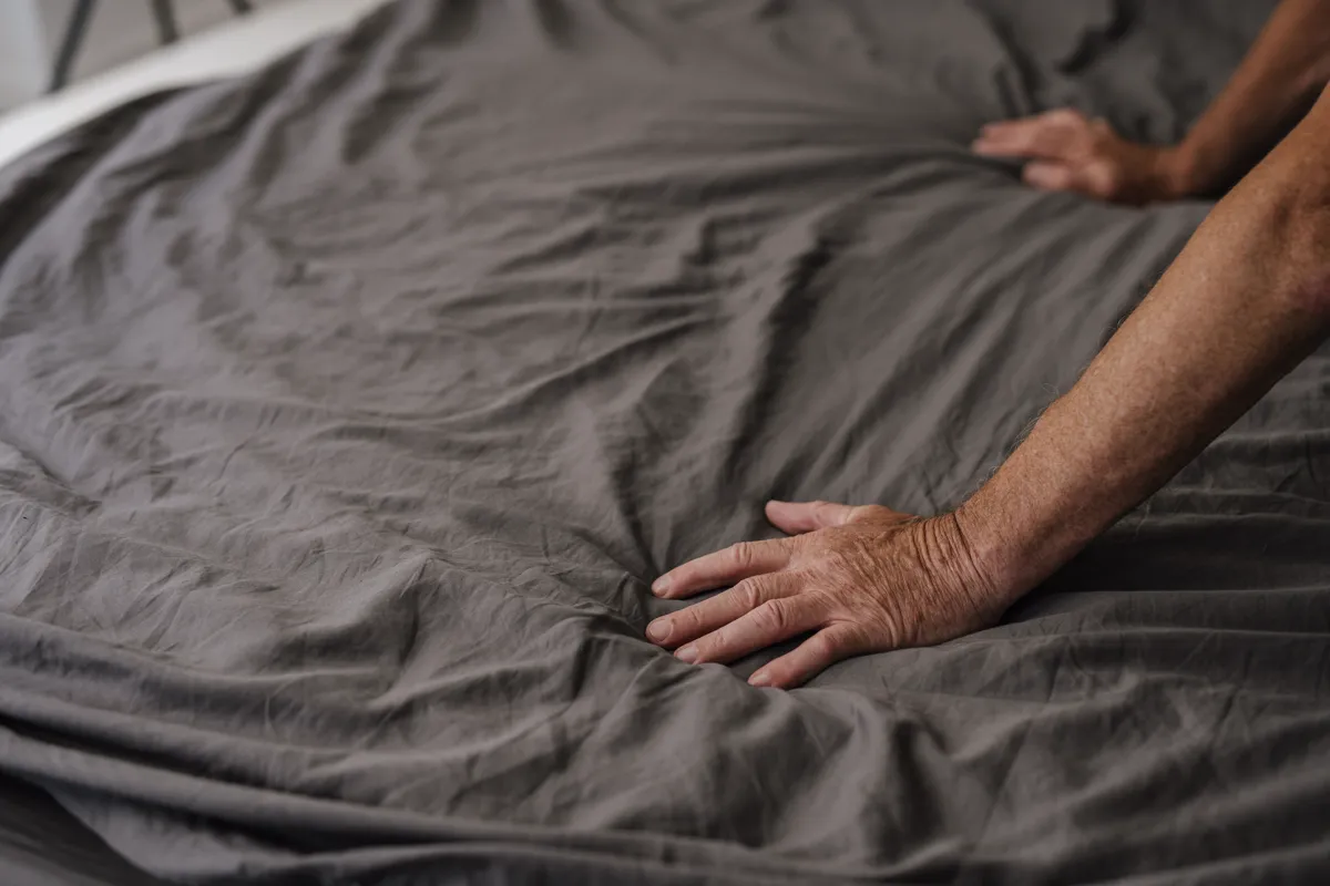 Mãos alisando um tecido de cama cinza